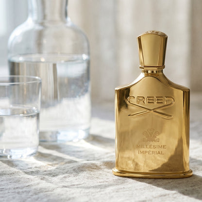 Creed Millesime Imperial on bleached canvas with a decanter of infused orange water