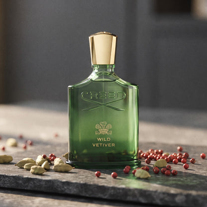 Creed Wild Vetiver EDP on dark grey stone slab with cardamom pods and pink peppercorns scattered