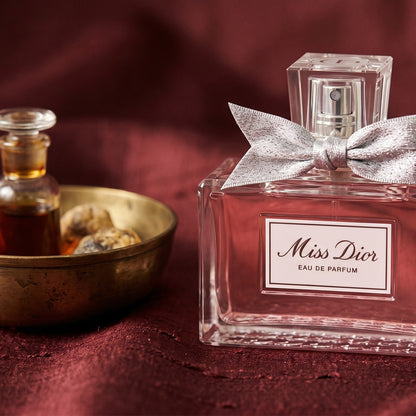 Dior Miss Dior on amber-toned satin with a gold-rim ceramic dish of labdanum