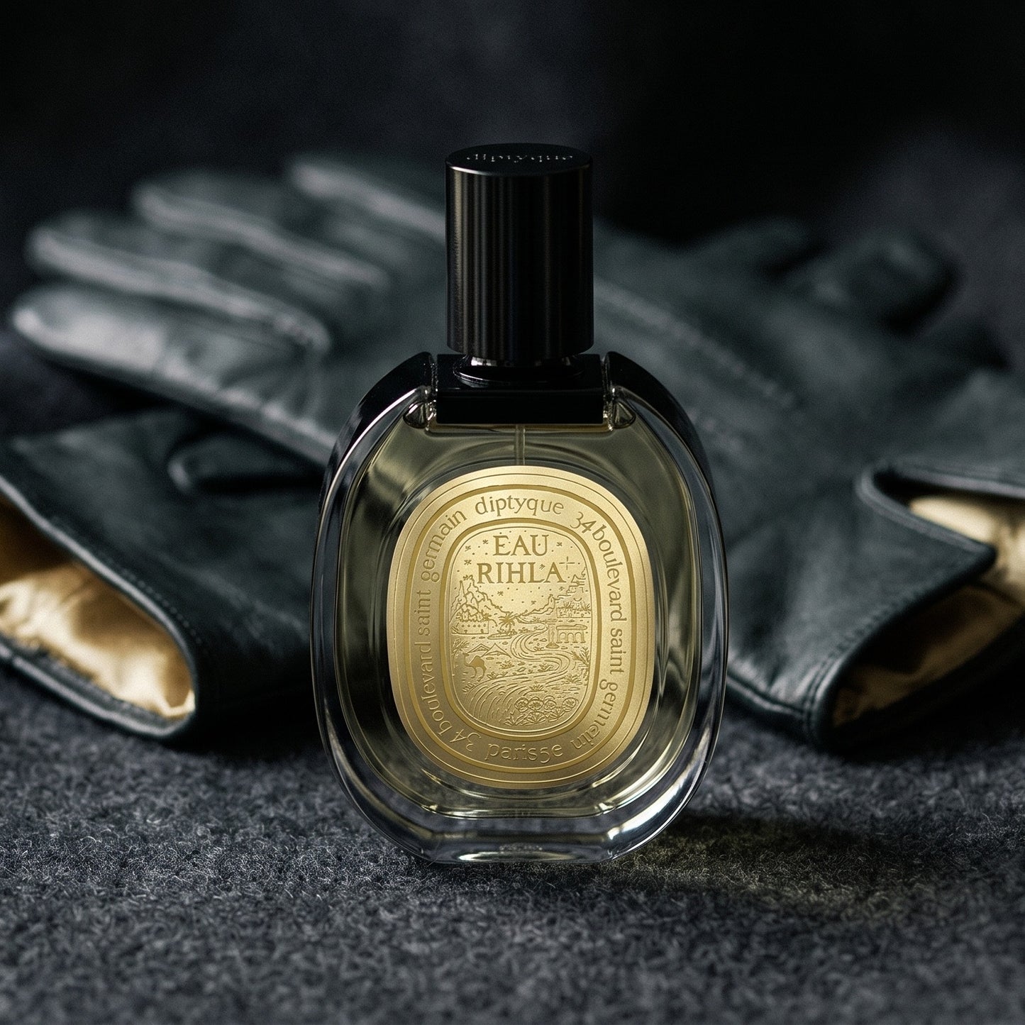 Diptyque Eau Rihla EDP on deep charcoal linen with a leather-strapped wristwatch lying flat