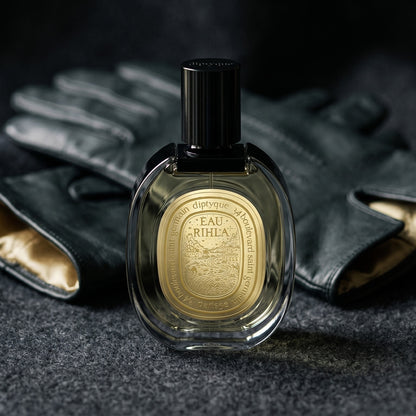 Diptyque Eau Rihla EDP on deep charcoal linen with a leather-strapped wristwatch lying flat
