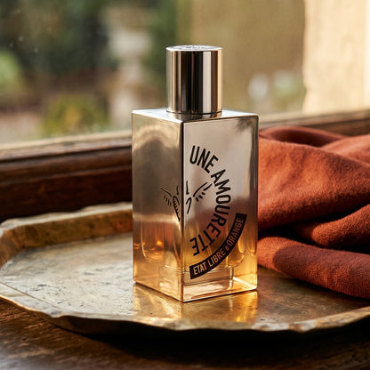 Etat Libre Une Amourette EDP on brass-edged surface with a silk-wool wrap in burnt sienna