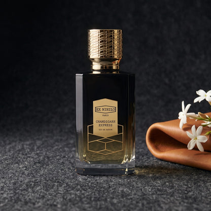 Ex Nihilo Chandigarh Express EDP on charcoal felt with a folded tan leather swatch with a sprig of jasmine resting against it