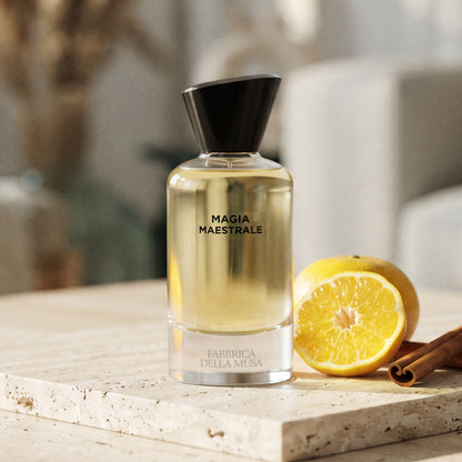 Fabbrica Della Musa Magia Maertrale EDP on pale travertine stone with a halved yellow mandarin and cinnamon sticks
