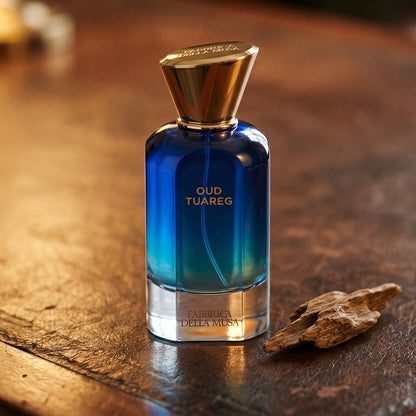 Fabbrica Della Musa Oud Tuareg Extrait de Parfum on aged leather-topped desk with a single agarwood chip beside the bottle