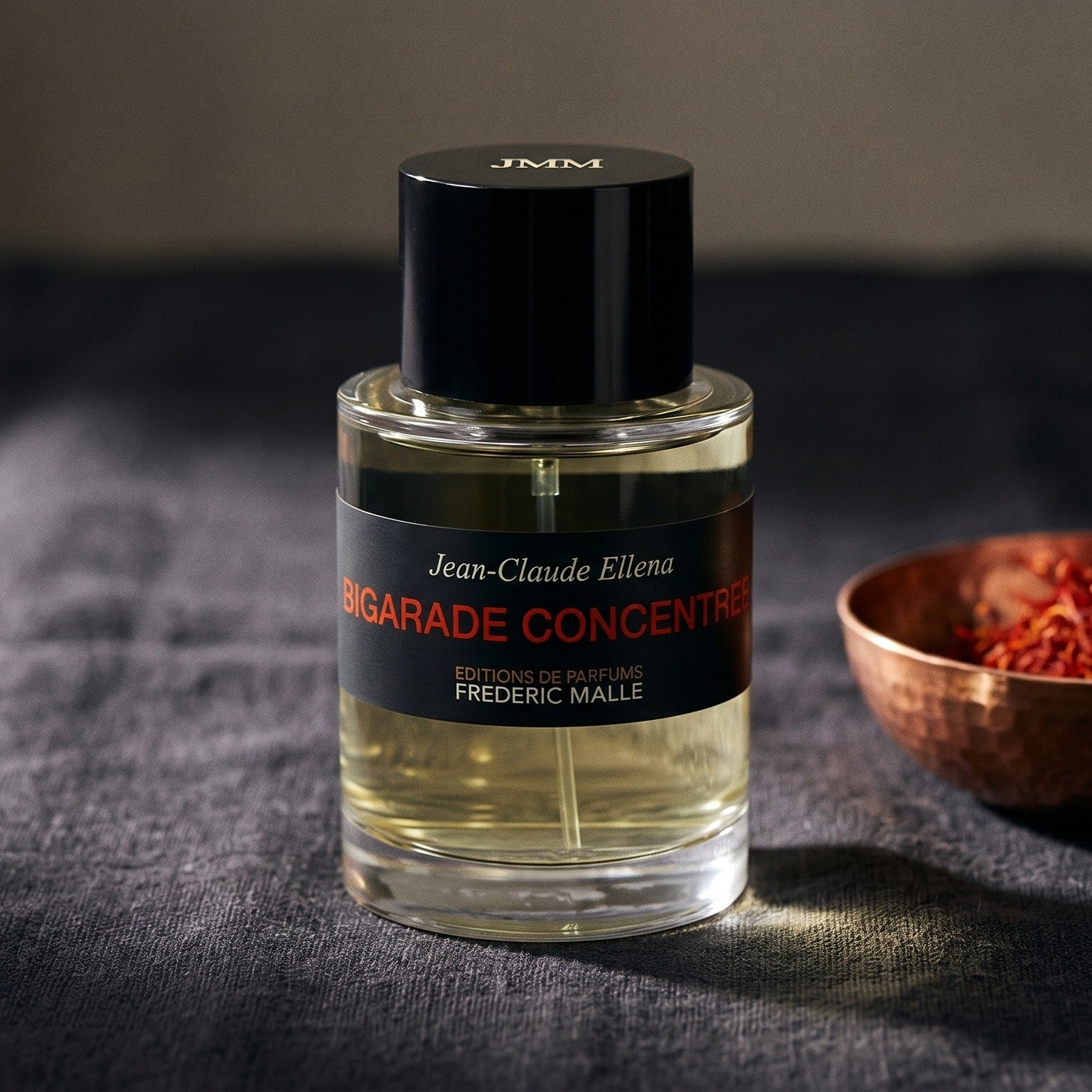Frederic Malle Bigarade Concentree EDT on slate-grey fabric with a pinch of black peppercorns scattered