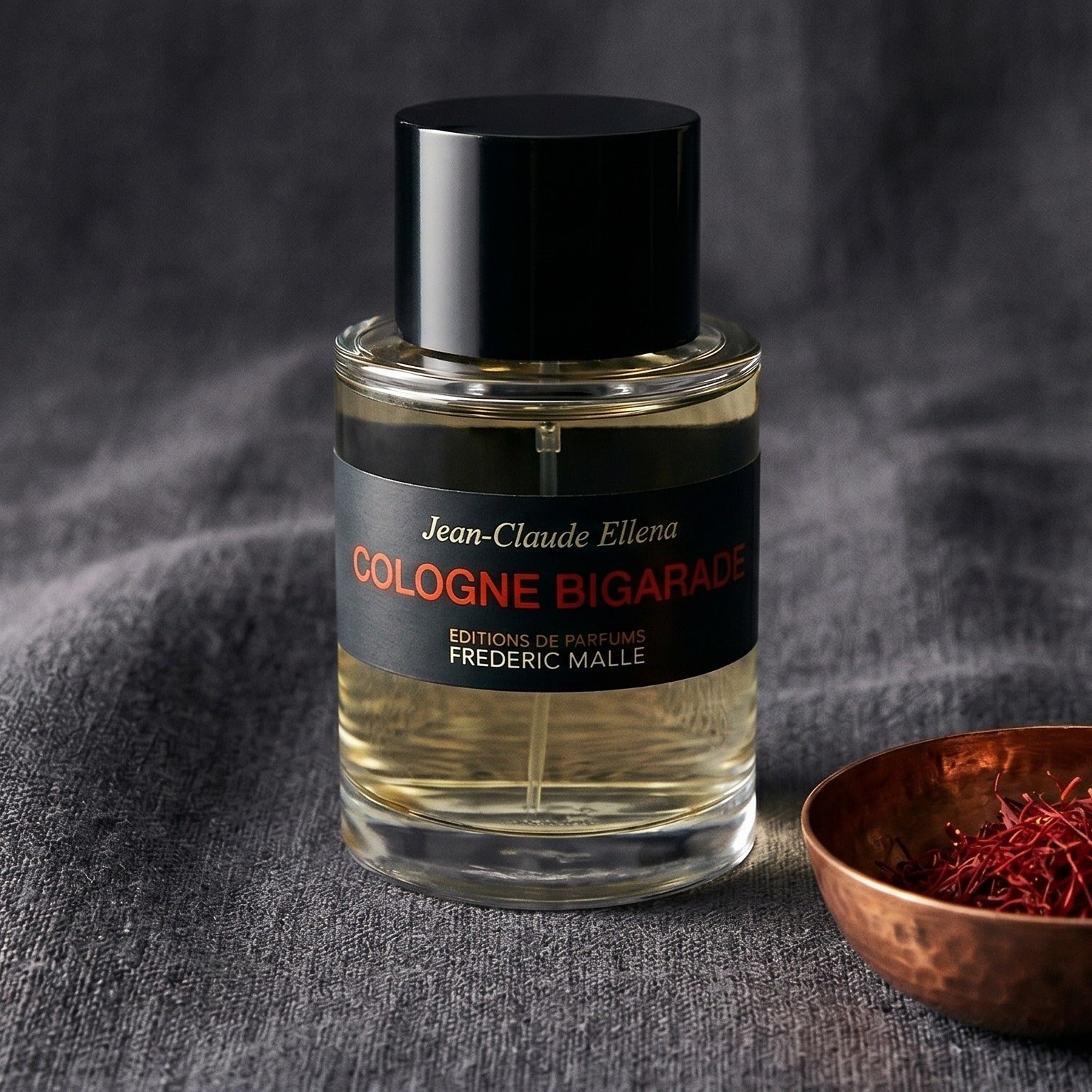 Frederic Malle Cologne Bigarade EDC on charcoal canvas with a scatter of dried cloves and cinnamon shards