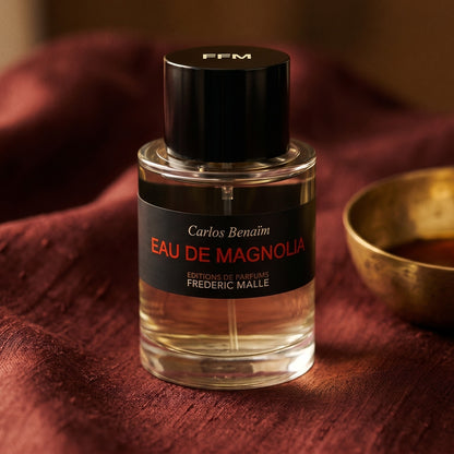 Frederic Malle Eau De Magnolia EDP on amber-toned satin with a gold-rim ceramic dish of labdanum