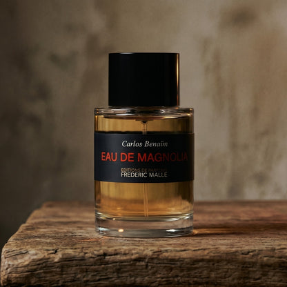 Frederic Malle Eau De Magnolia EDP on walnut side table with a pair of lit votives beside the bottle
