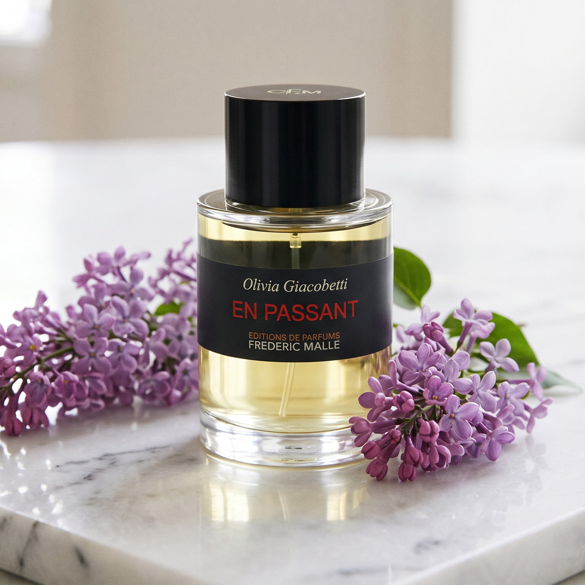 Frederic Malle En Passant EDP on white marble with a few sprigs of purple lilac