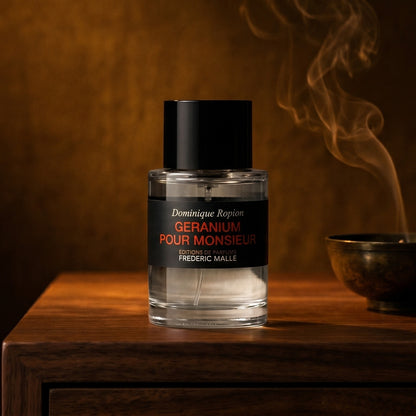 Frederic Malle Geranium Pour Monsieur EDP on smoked-glass tabletop with a lacquered incense burner in mid-glow