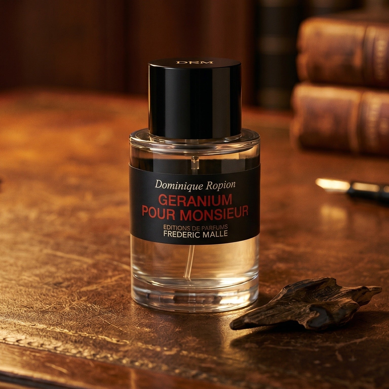 Frederic Malle Geranium Pour Monsieur EDP on dark tan leather desk with a brass lamp casting a warm pool of light