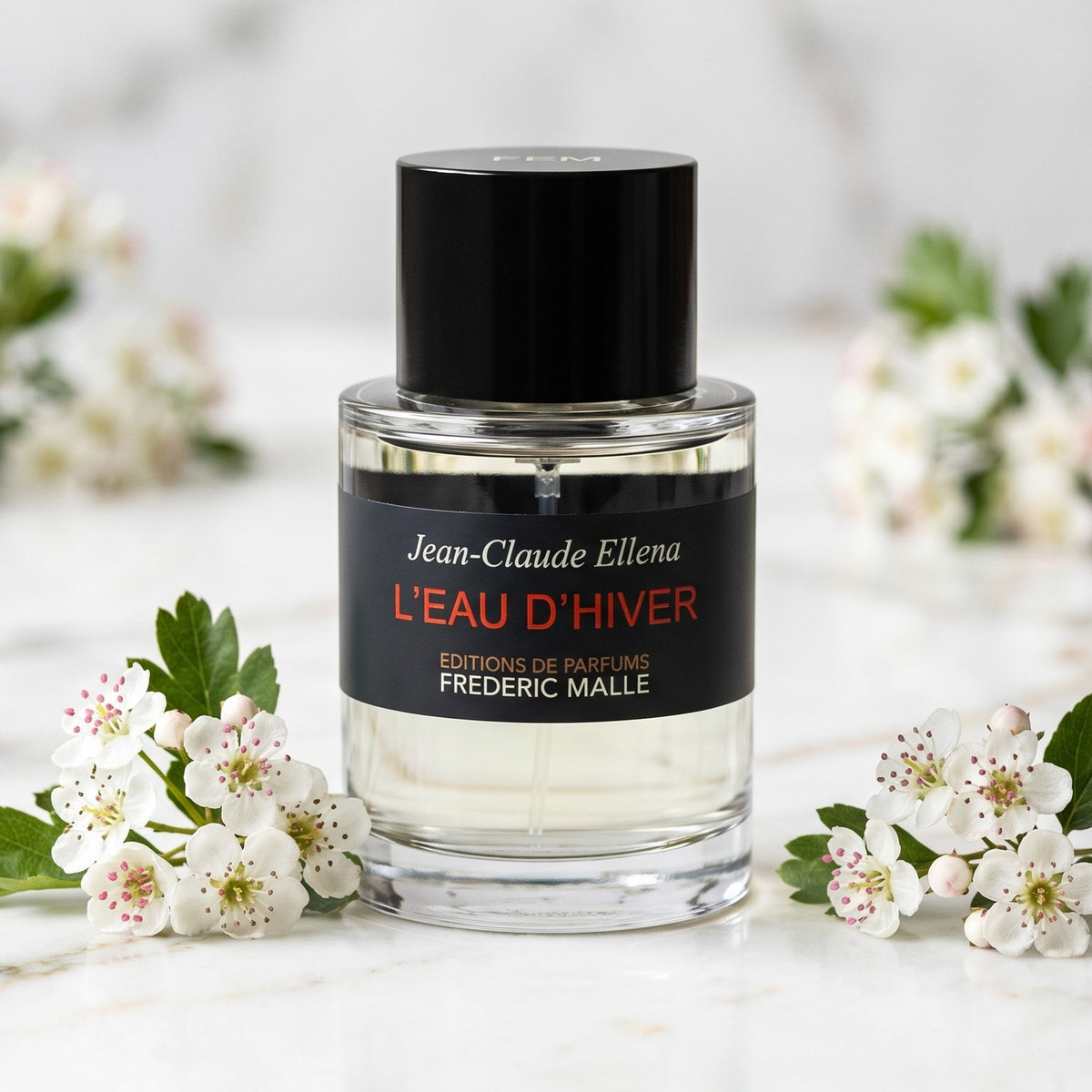 Frederic Malle L'Eau D'Hiver EDT on white marble with a few sprigs of hawthorn blossom