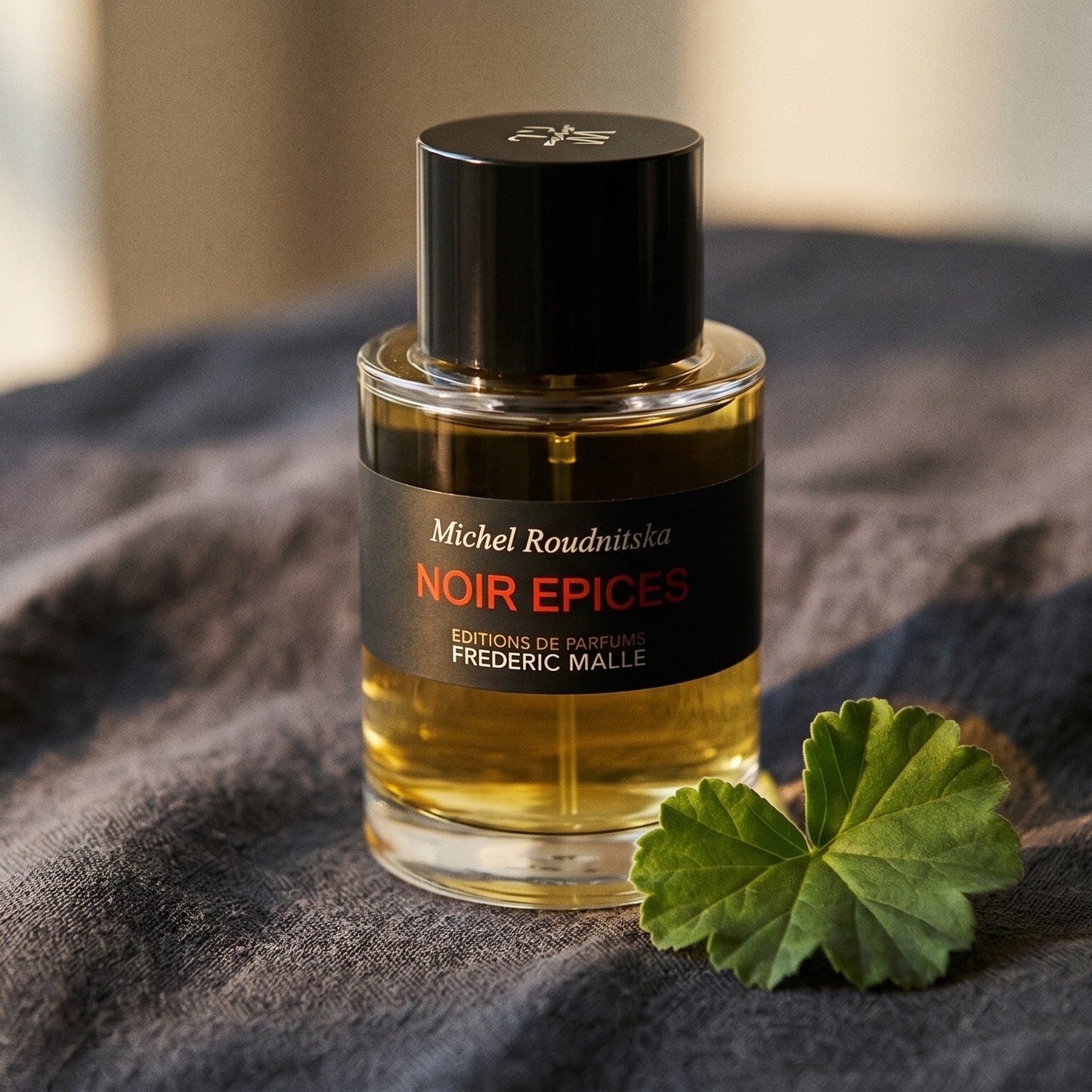 Frederic Malle Noir Epices EDP on charcoal linen with a geranium leaf