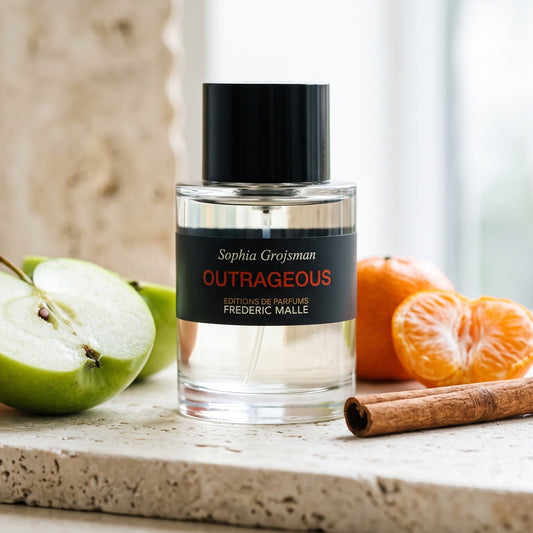 Frederic Malle Outrageous EDT on pale travertine with a halved green apple beside halved mandarins and a cinnamon stick