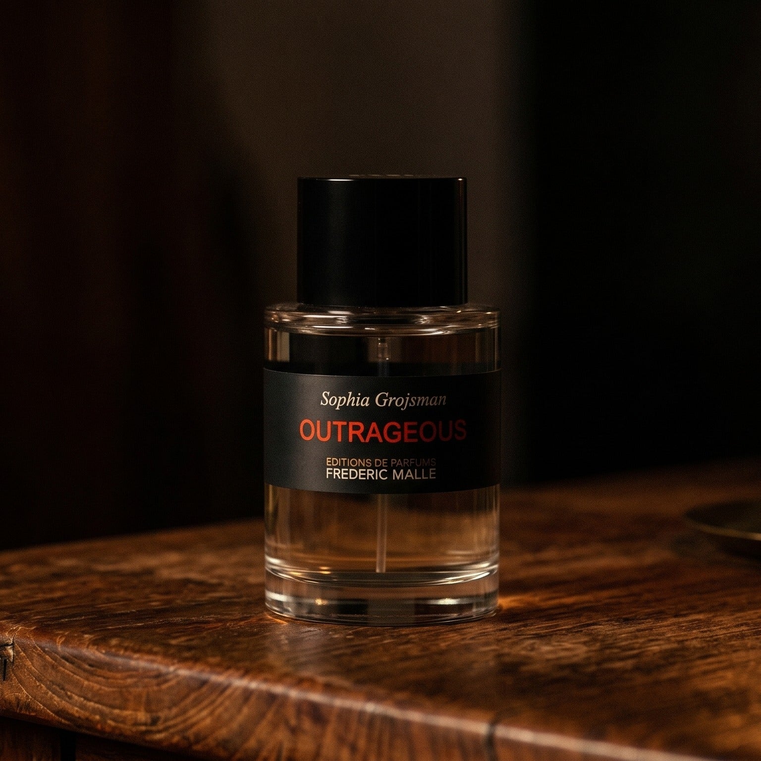 Frederic Malle Outrageous EDP on dark cherrywood with a tall beeswax taper casting warm light