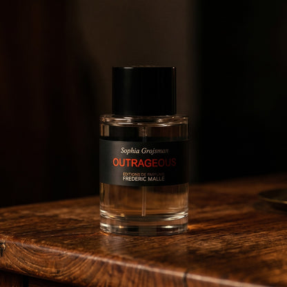 Frederic Malle Outrageous EDP on dark cherrywood with a tall beeswax taper casting warm light