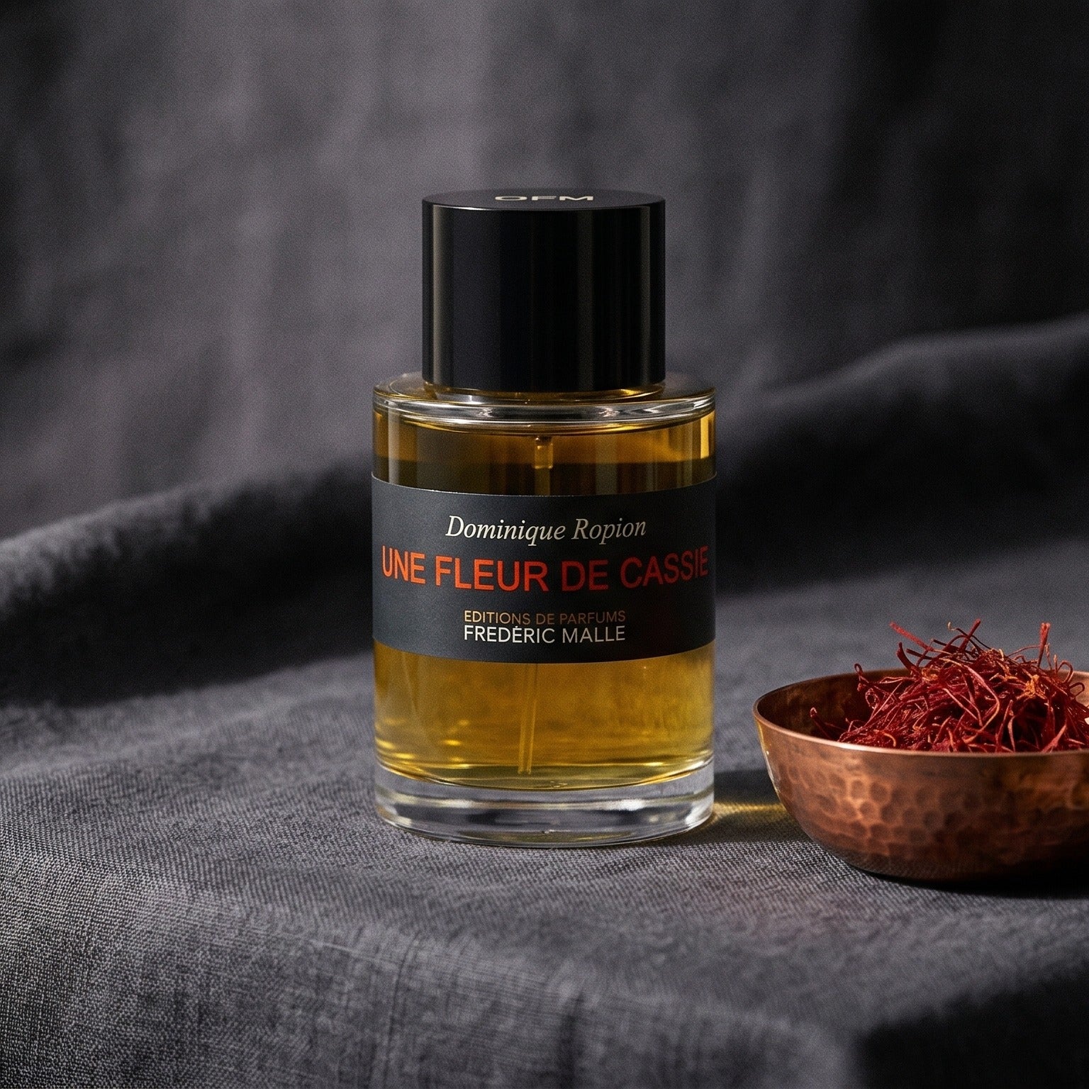 Frederic Malle Une Fleur De Cassie EDP on charcoal canvas with a scatter of dried cloves and cinnamon shards