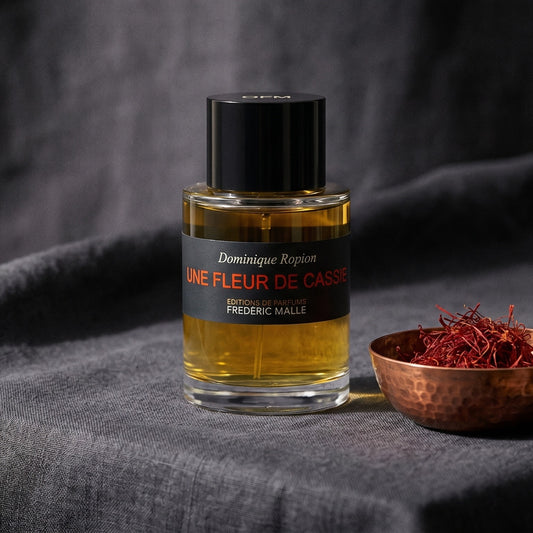 Frederic Malle Une Fleur De Cassie EDP on charcoal canvas with a scatter of dried cloves and cinnamon shards