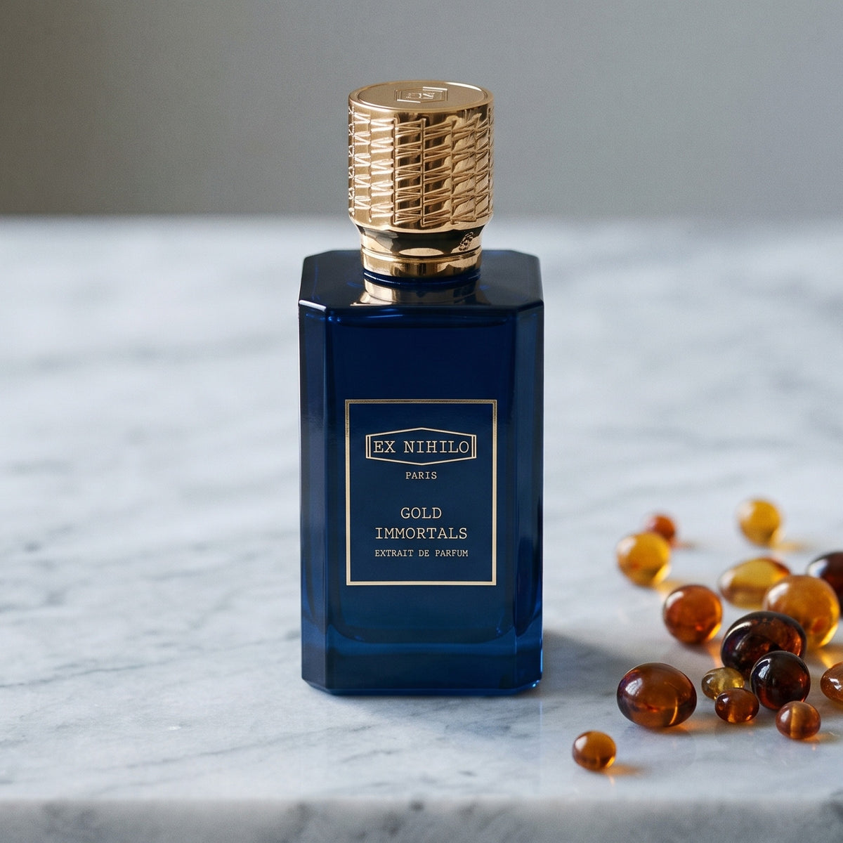 Ex Nihilo Gold Immortals Extrait de Parfum on pale grey marble with amber resin beads scattered to one side