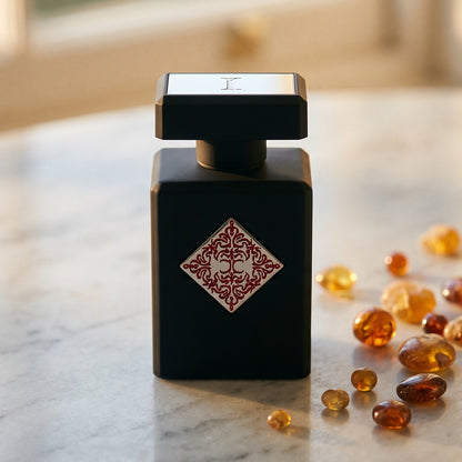Initio Divine Attraction EDP on cream stone with a scatter of honey-colored ambergris flakes