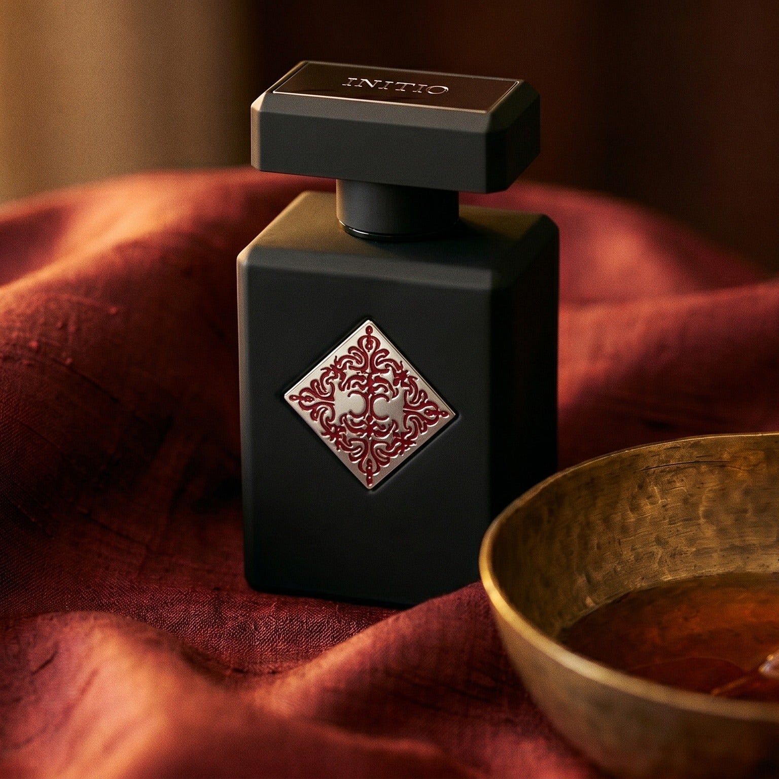 Initio Divine Attraction EDP on deep caramel velvet with a small copper jar of resin balm