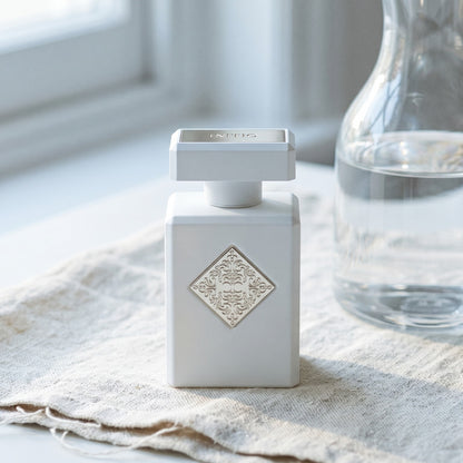 Initio Musk Therapy EDP on white linen with a cut-crystal pitcher and a slice of lemon