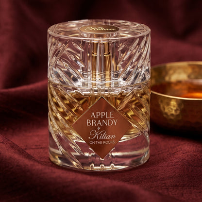 Kilian Apple Brandy on the Rocks on russet silk with a matte brass bowl holding tonka and amber pieces