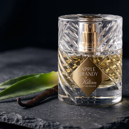 Kilian Apple Brandy on the Rocks on dark slate with a pineapple crown leaf beside a vanilla pod