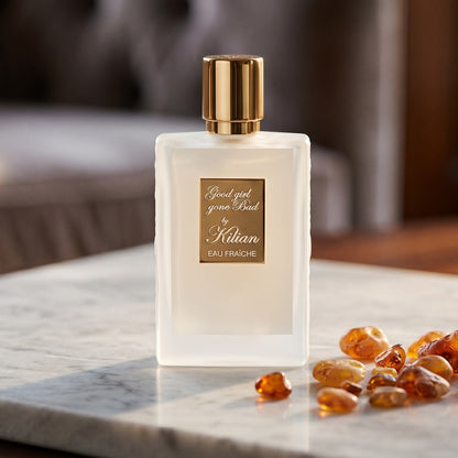 Kilian Good Girl Gone Bad EDP on cream stone with a scatter of honey-colored ambergris flakes