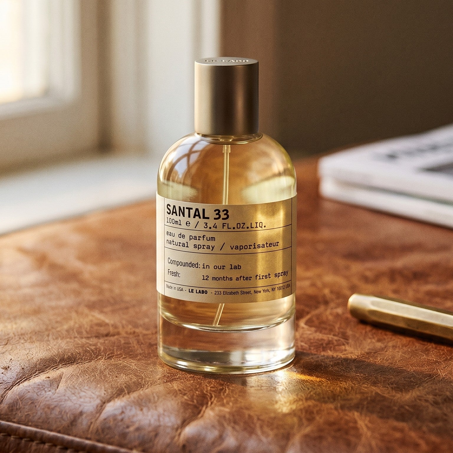 Le Labo Santal 33 on aged cognac-leather surface with a brass fountain pen resting beside the bottle
