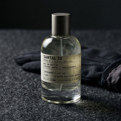 Le Labo Santal 33 EDP on charcoal felt with a silk-lined glove just behind the bottle