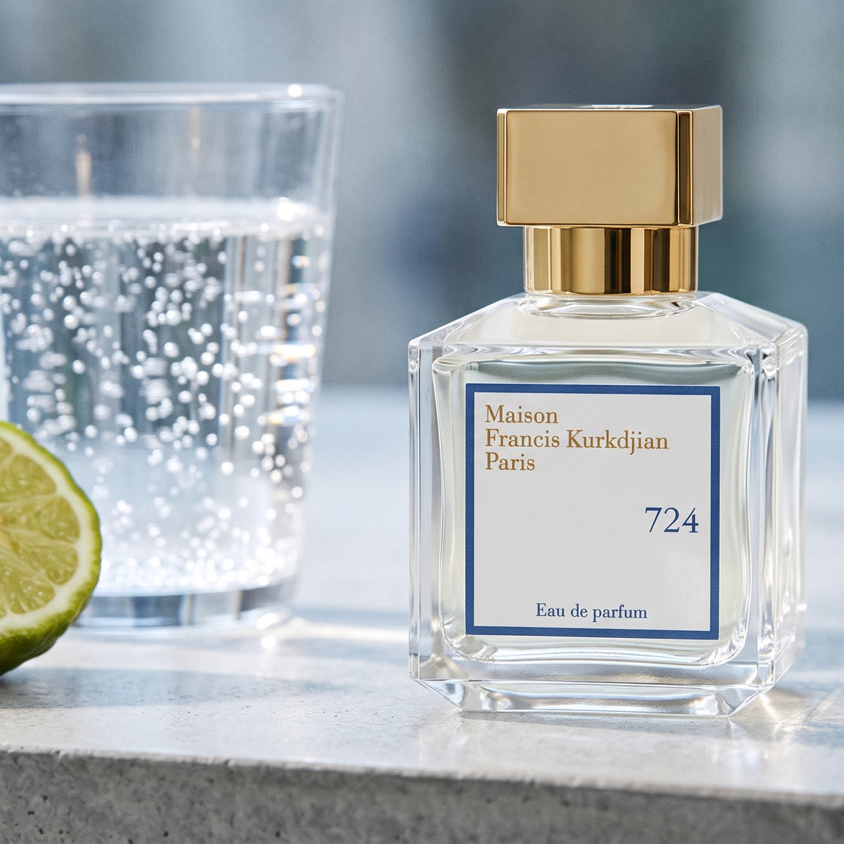Maison Francis Kurkdjian (MFK) 724 EDP on pale grey polished concrete with a halved bergamot and sparkling water