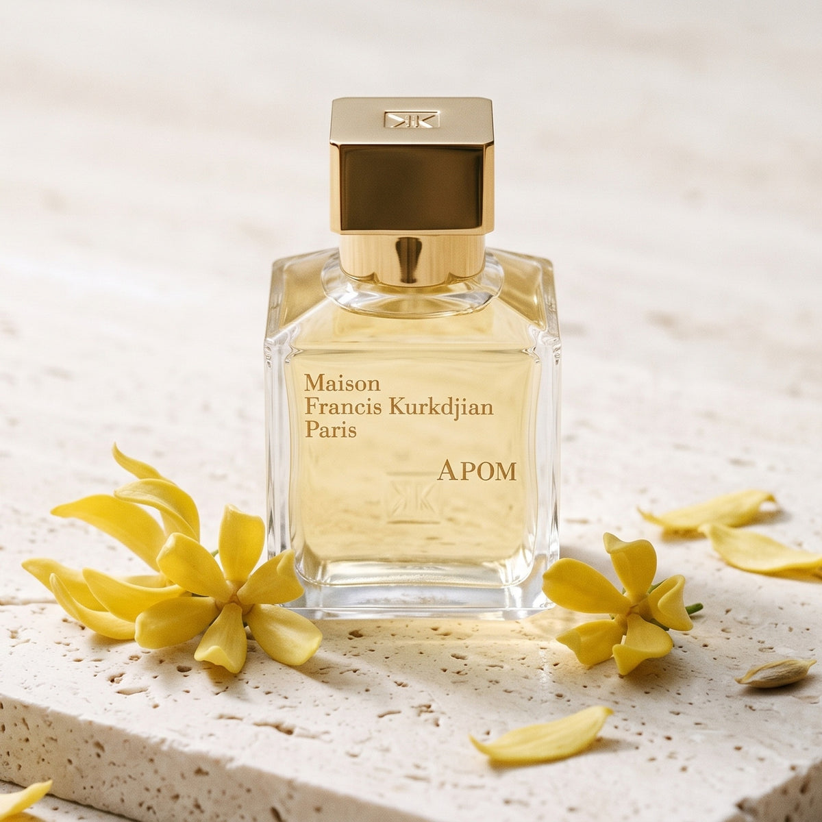 Maison Francis Kurkdjian (MFK) Apom EDP on pale travertine with a few ylang-ylang flowers