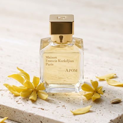 Maison Francis Kurkdjian (MFK) Apom EDP on pale travertine with a few ylang-ylang flowers