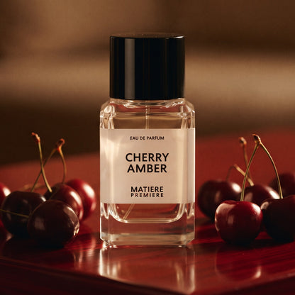 Matiere Premiere Cherry Amber EDP on dark red lacquered wood with fresh cherries