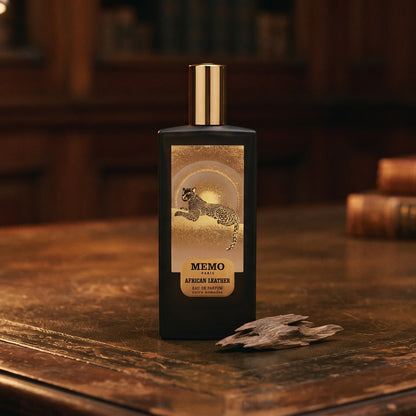 Memo Paris African Leather EDP on aged leather-topped desk with a single agarwood chip beside the bottle