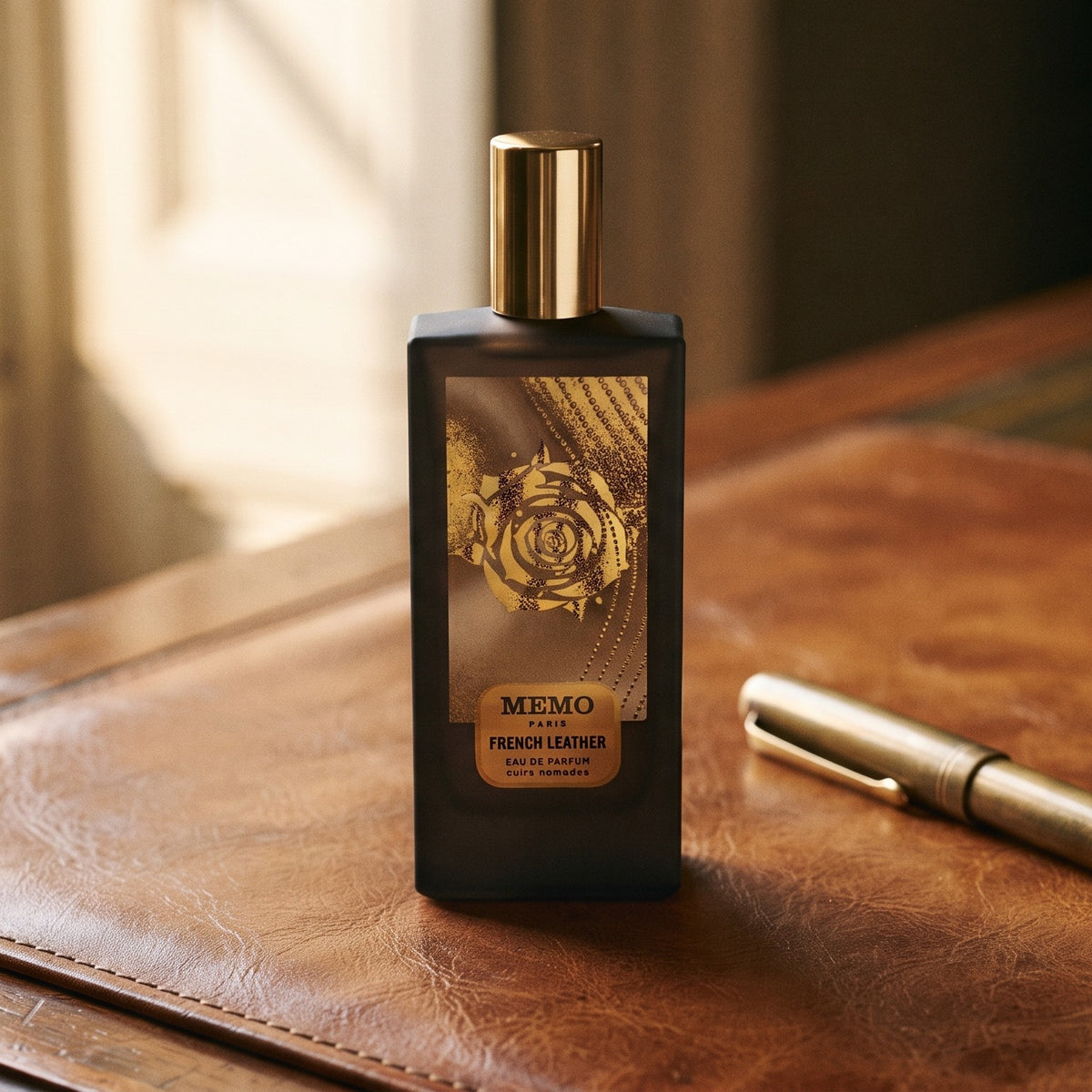 Memo Paris French Leather EDP on aged cognac-leather surface with a brass fountain pen resting beside the bottle