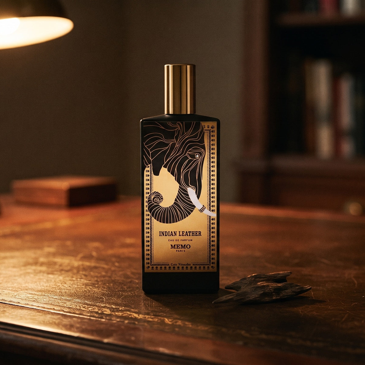 Memo Paris Indian Leather EDP on aged leather-topped desk with a single agarwood chip beside the bottle