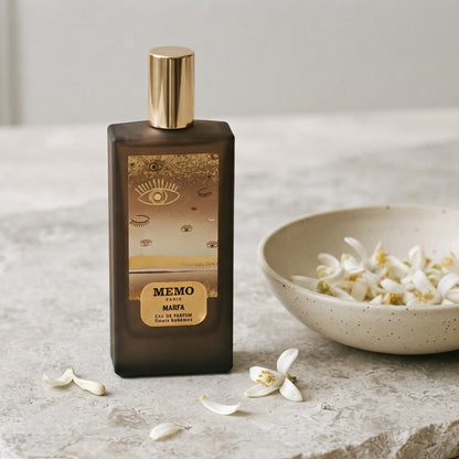 Memo Paris Marfa EDP on pale stone with orange-blossom petals in a shallow bowl