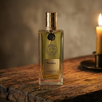 Nicolai Patchouli Intense EDP on rosewood surface with a squat brass candle flickering nearby