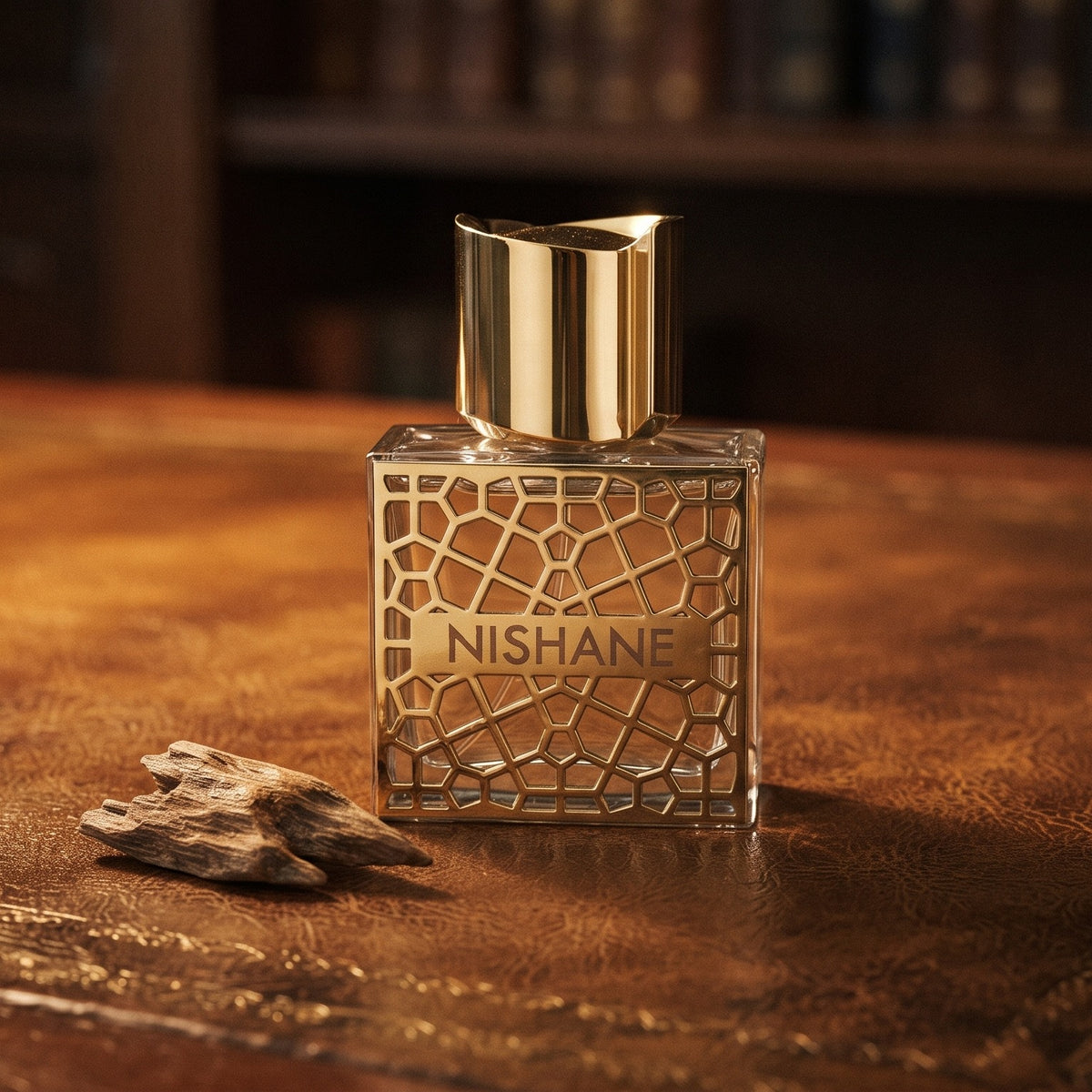 Nishane Hacivat Oud Extrait de Parfum on aged leather-topped desk with a single agarwood chip beside the bottle