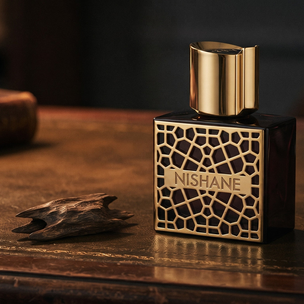 Nishane Mana Extrait de Parfum on aged leather-topped desk with a single agarwood chip beside the bottle