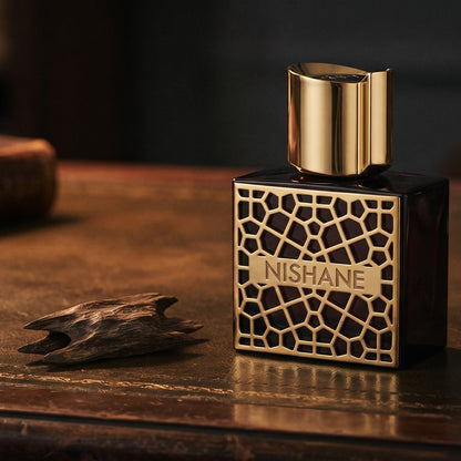 Nishane Mana Extrait de Parfum on aged leather-topped desk with a single agarwood chip beside the bottle