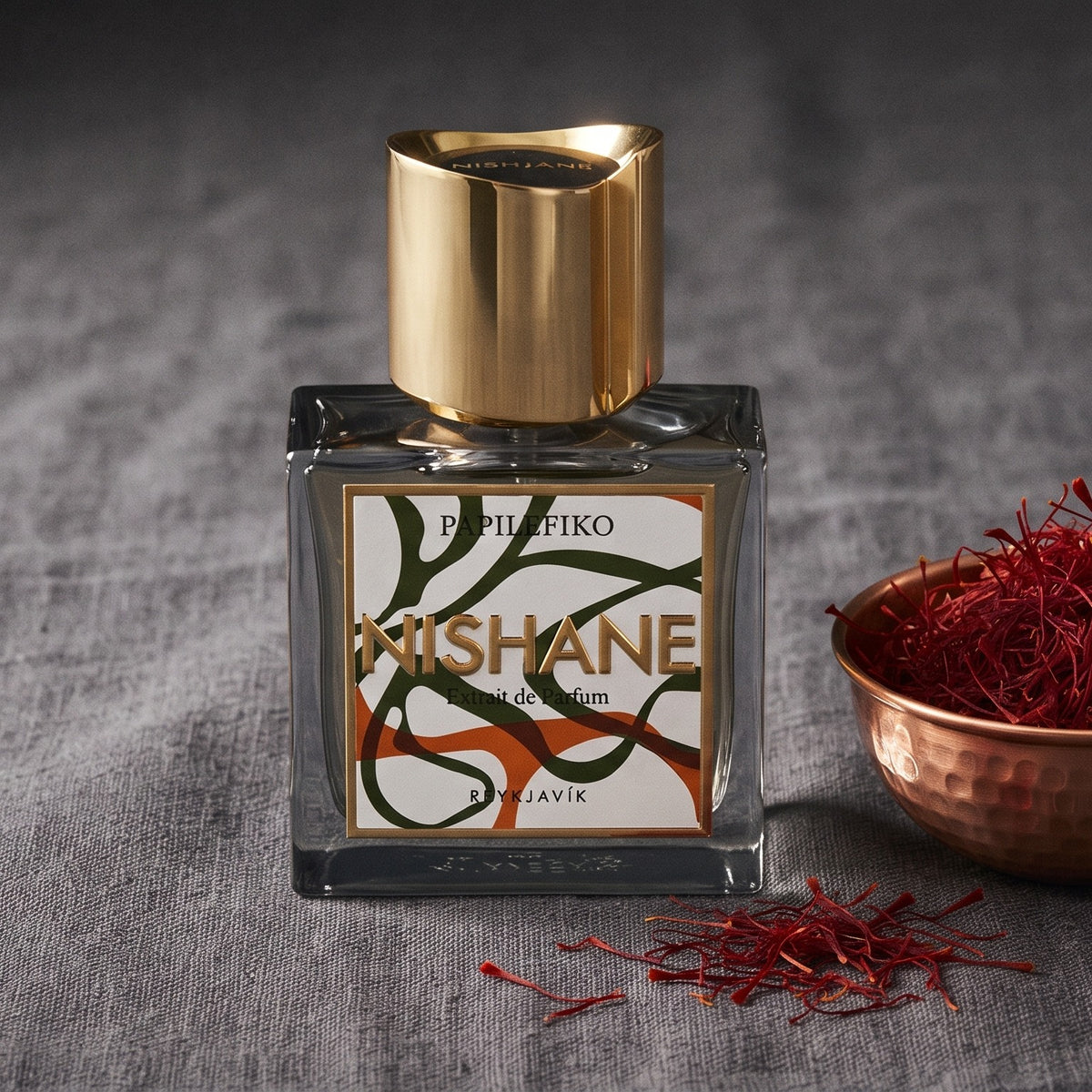 Nishane Papilefiko Extrait de Parfum on charcoal linen with a small copper bowl of saffron threads