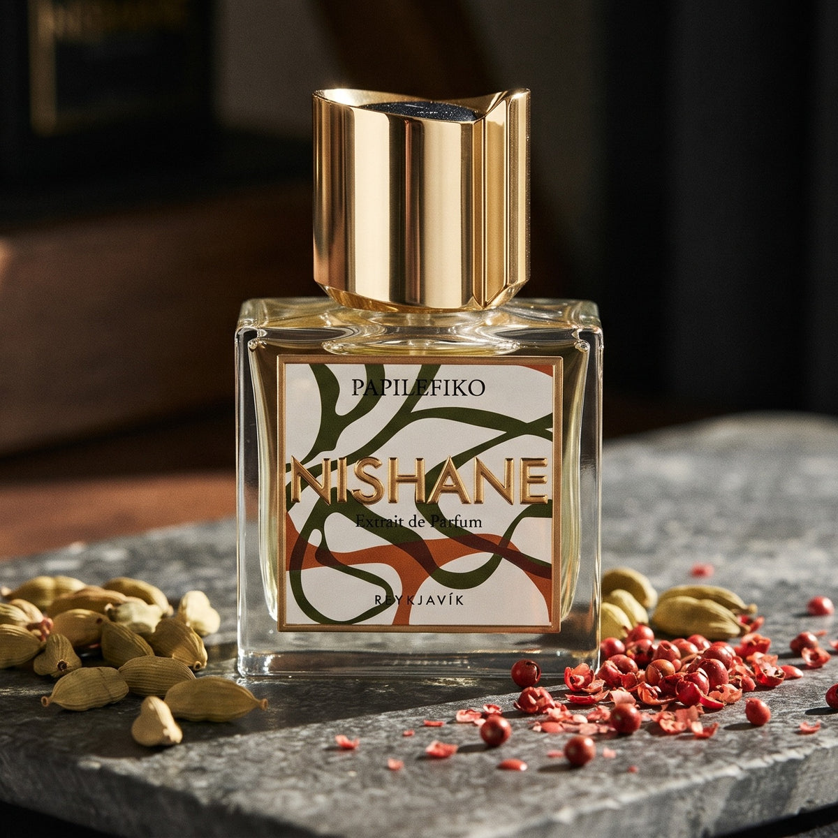 Nishane Papilefiko Extrait de Parfum on dark grey stone slab with cardamom pods and pink peppercorns scattered