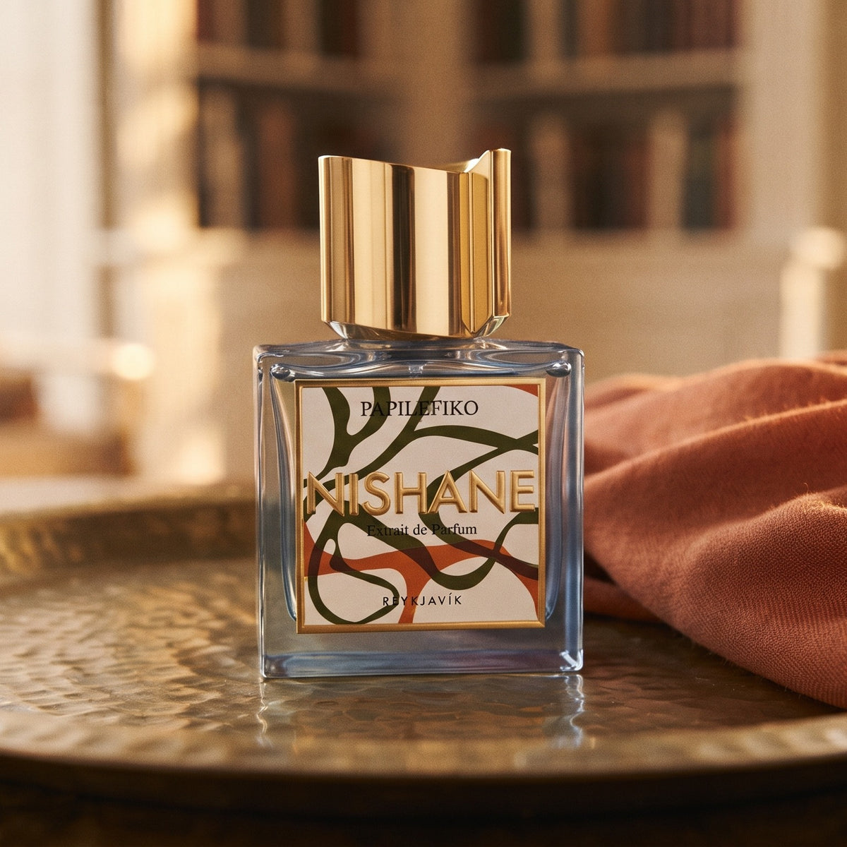 Nishane Papilefiko Extrait de Parfum on aged brass tray with a folded pashmina in rust tone