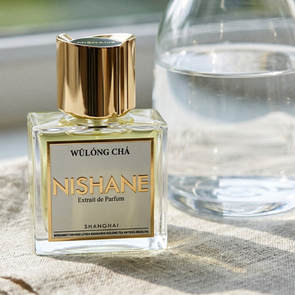 Nishane Wulong Cha EDP on pale flax fabric with a glass jar of bergamot essence
