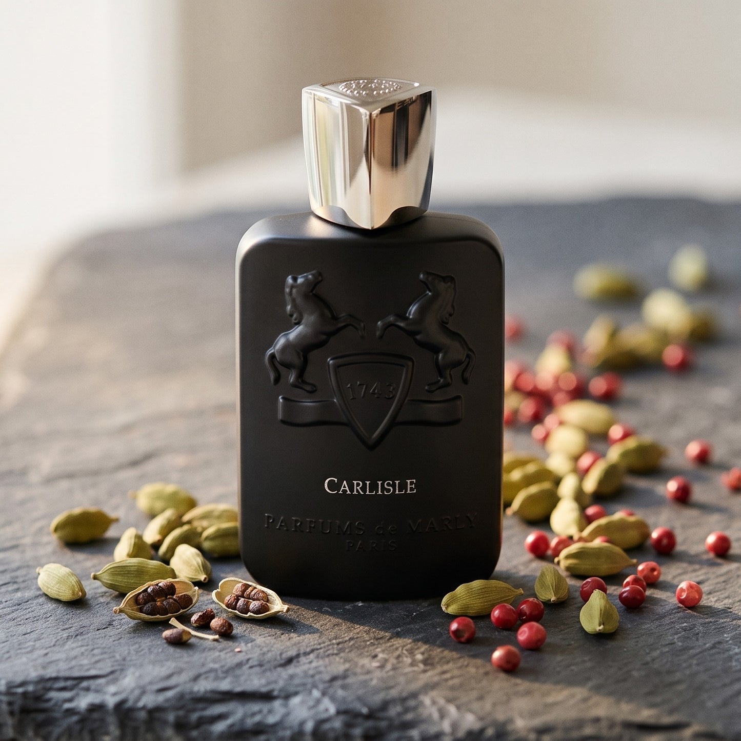 Parfums de Marly Carlisle EDP on dark grey stone slab with cardamom pods and pink peppercorns scattered