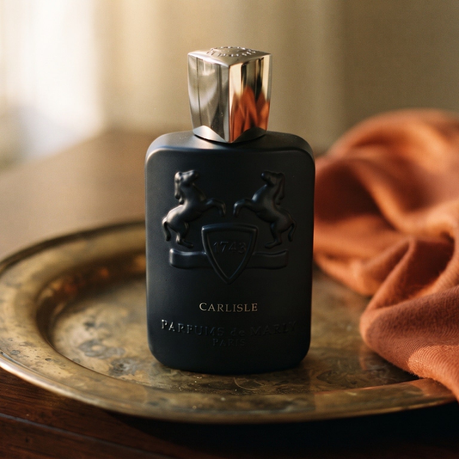 Parfums de Marly Carlisle EDP on aged brass tray with a folded pashmina in rust tone